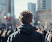 A teenager wearing a hooded jacket is standing in a busy city street, looking ahead.