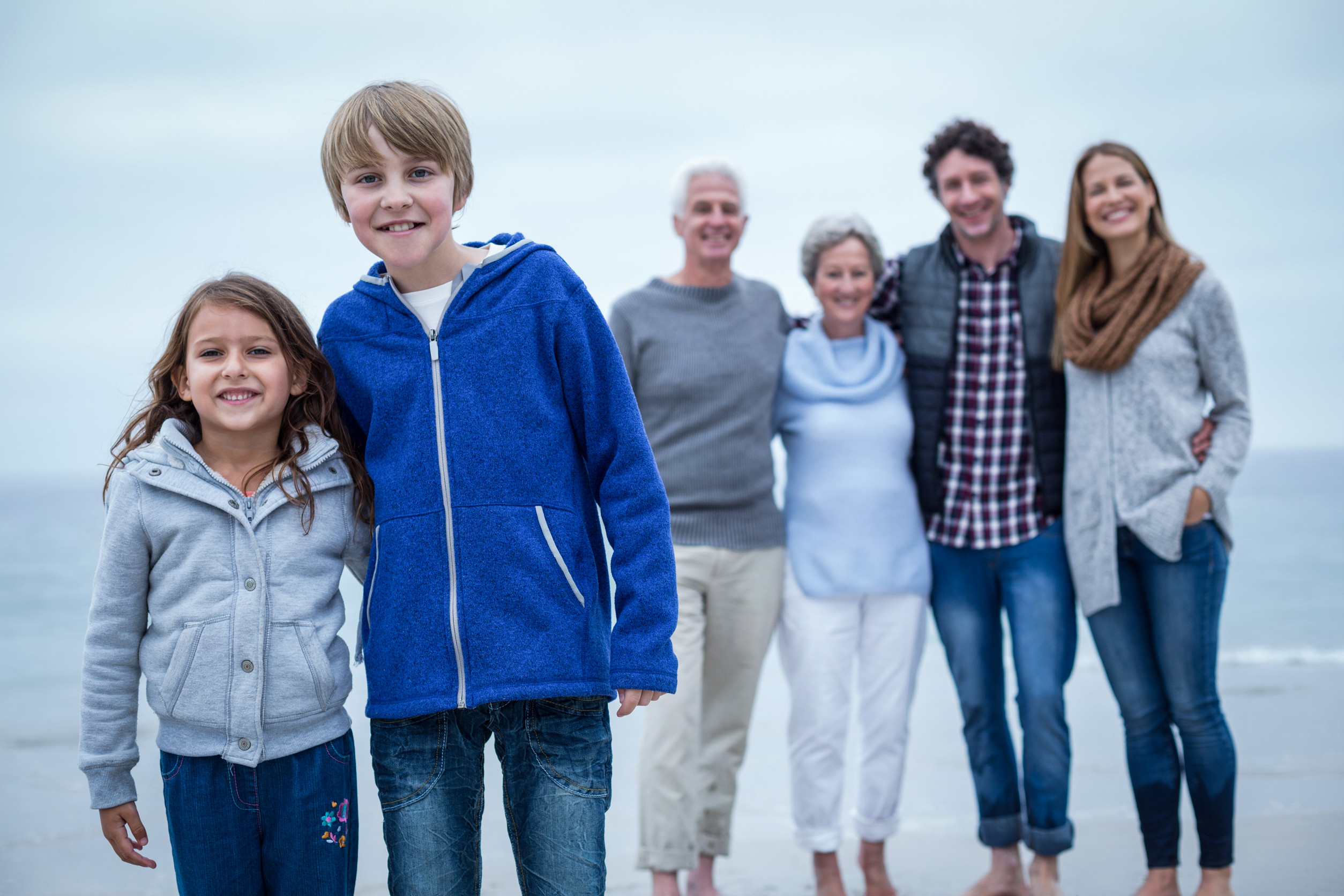  Smiling family standing together on a beach, with two children in the front and adults in the background.