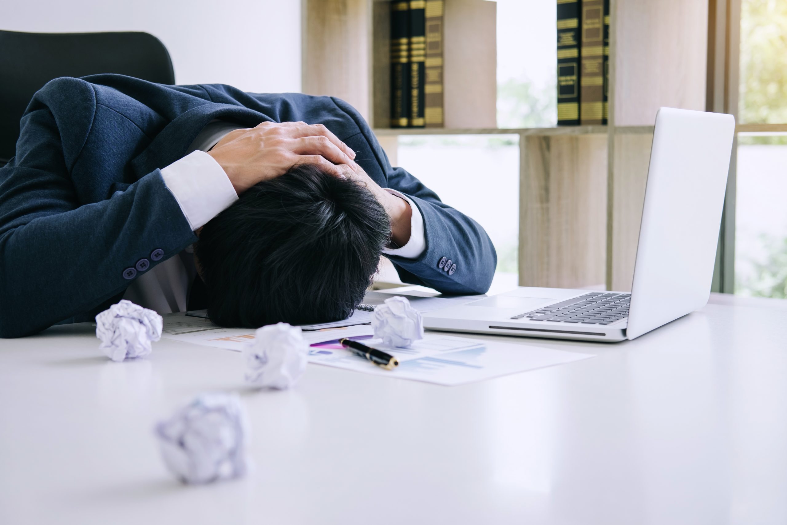 Feeling stress and headache, Businessman depressed and exhausted at his desk frustrated with problems with a pile of work while hiding his face on table