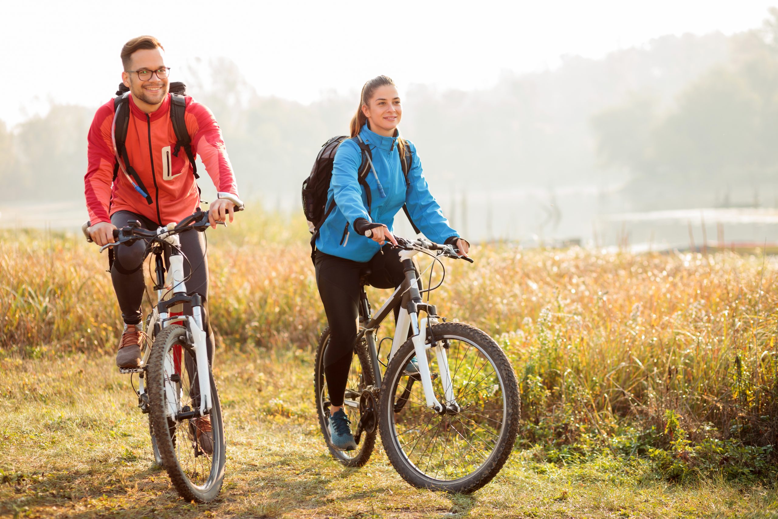 Beautiful happy young couple enjoying early morning bicycle ride by the river or lake. Sunrise through the mist above water in the background