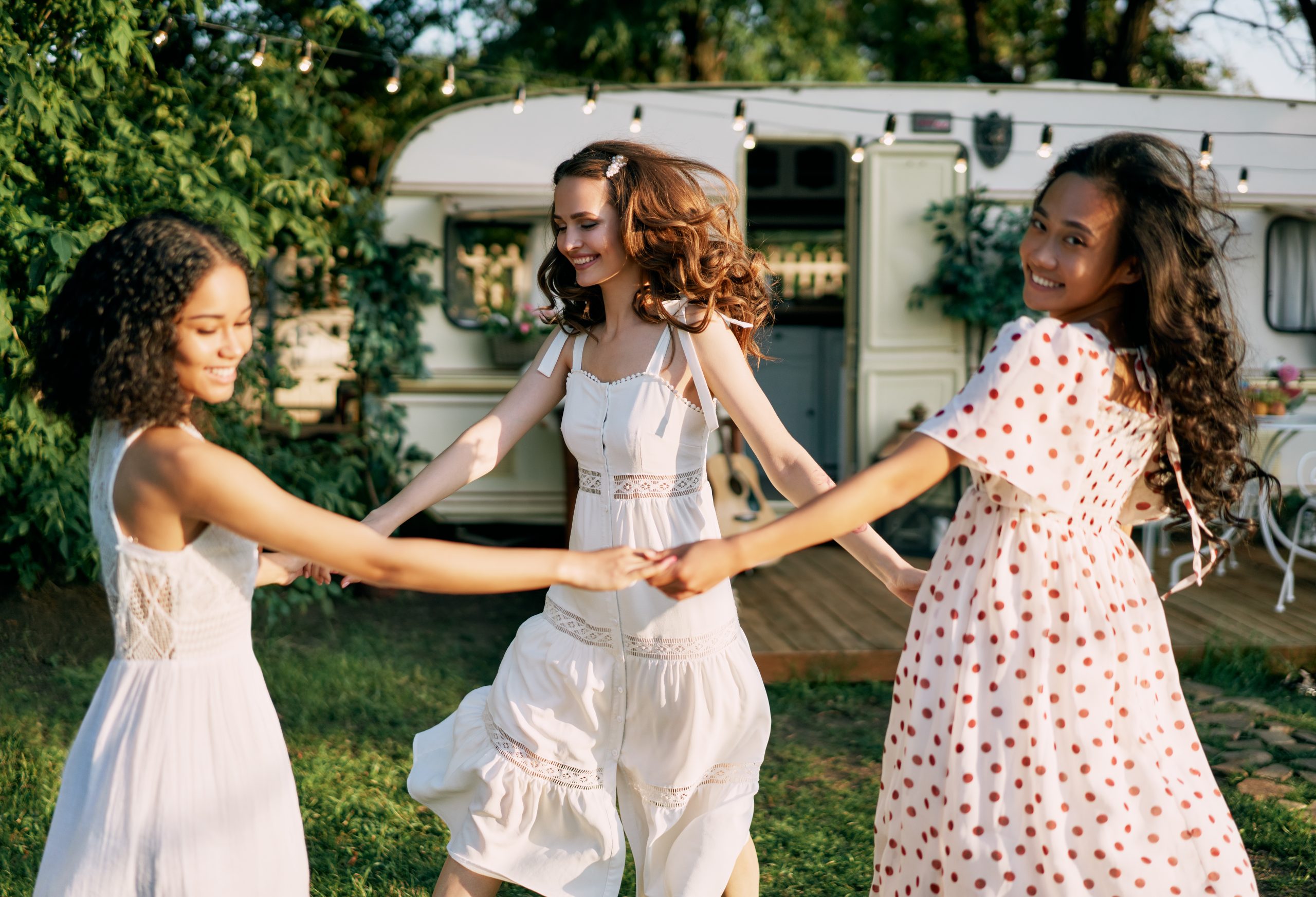 Three smiling women dancing in circle during picnic