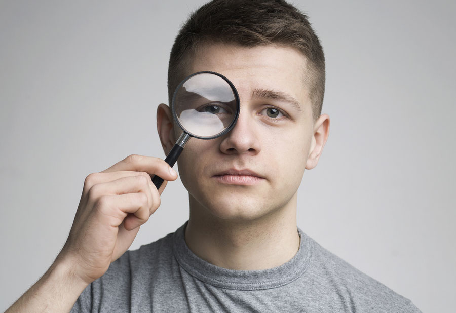 Young Man With Magnifying Glass Near Eye, Close Up