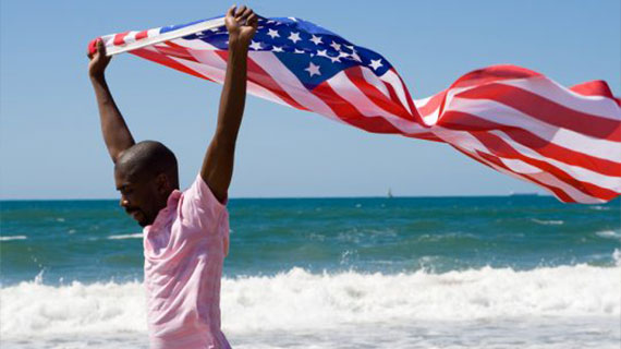 Young African American man waving a USA flag on beach
