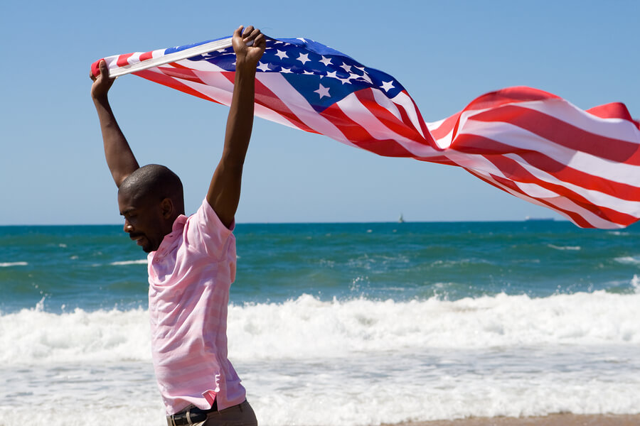 young african american man waving a USA flag on beach