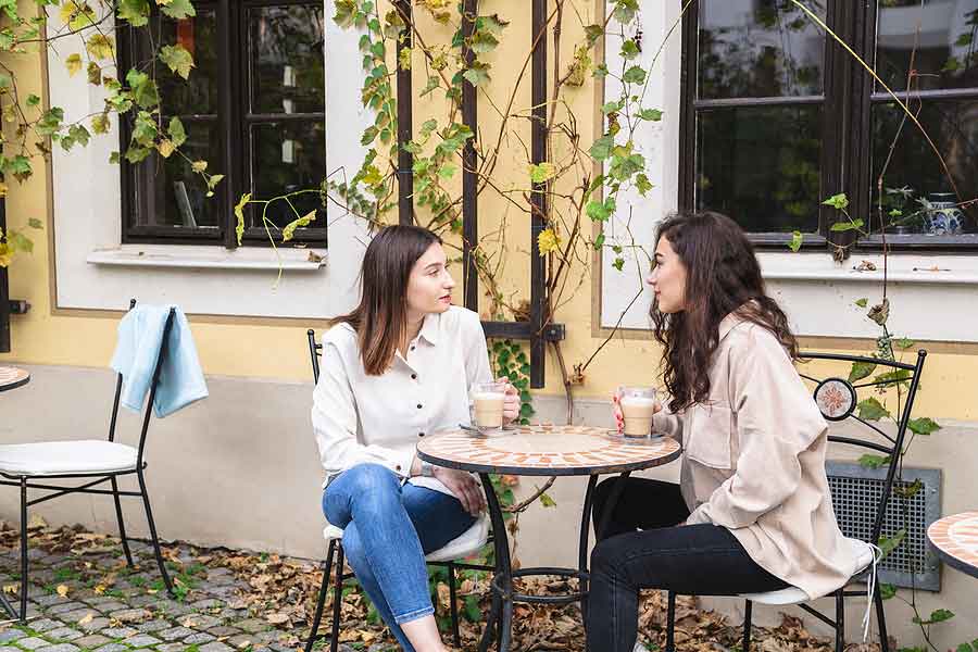 Two Young Women Talk And Drink Coffee In Cafe