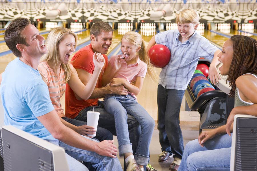 Families In Bowling Alley With Two Friends Cheering And Smiling