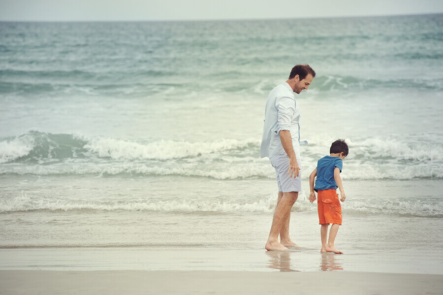 Father and son at beach holding hands looking at the ocean toget