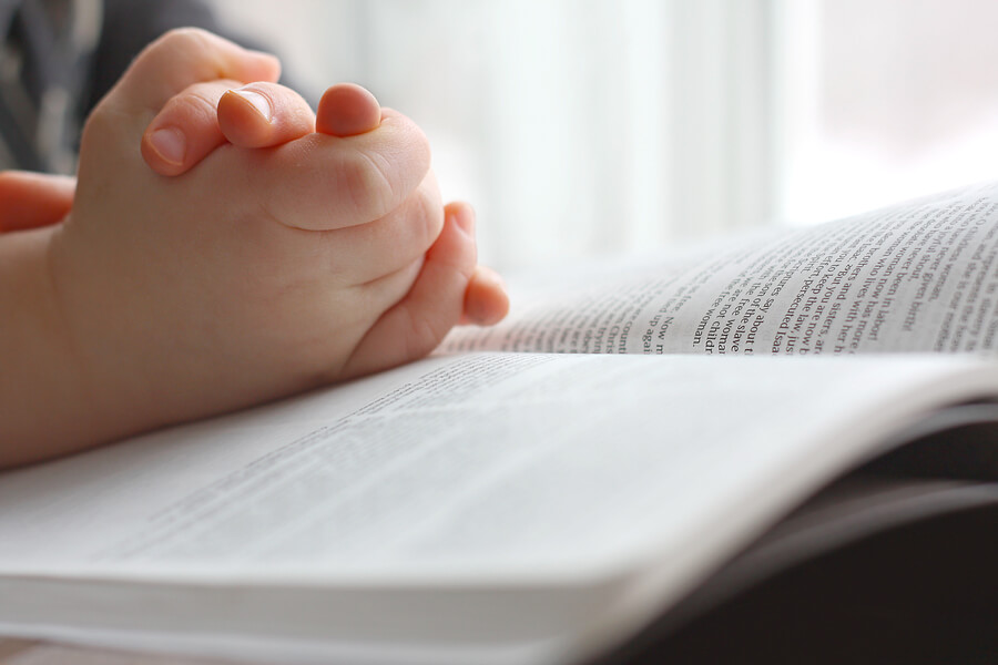 Young Child's Hands Praying On Holy Bible