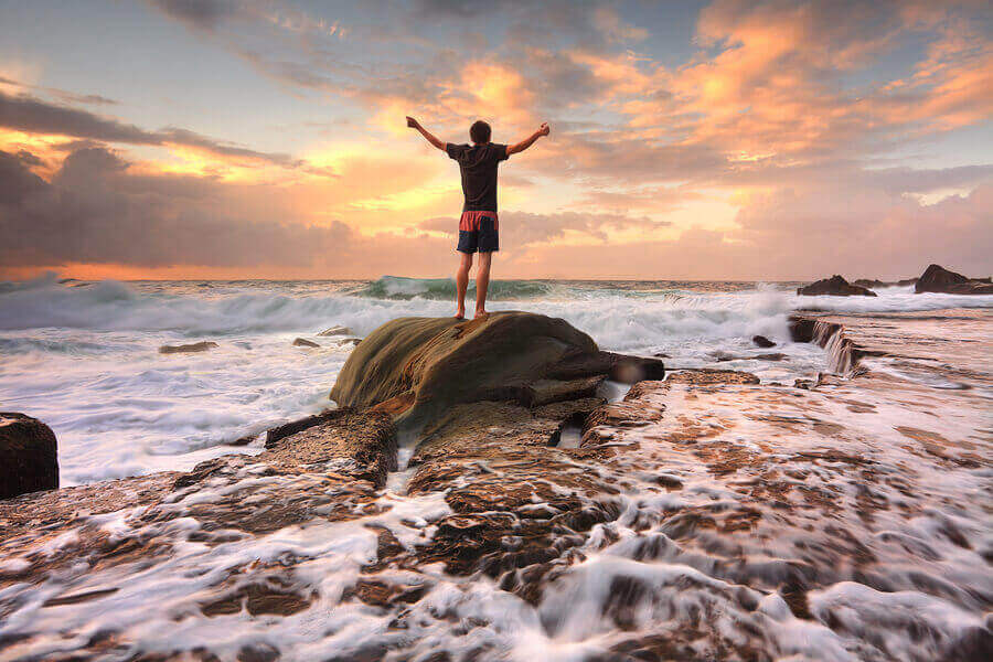 Teen boy stands on a rock among turbulent ocean seas