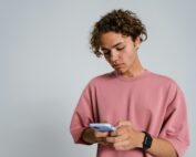Adolescent boy looking down at his smartphone, illustrating how digital overstimulation impacts teen behavior.