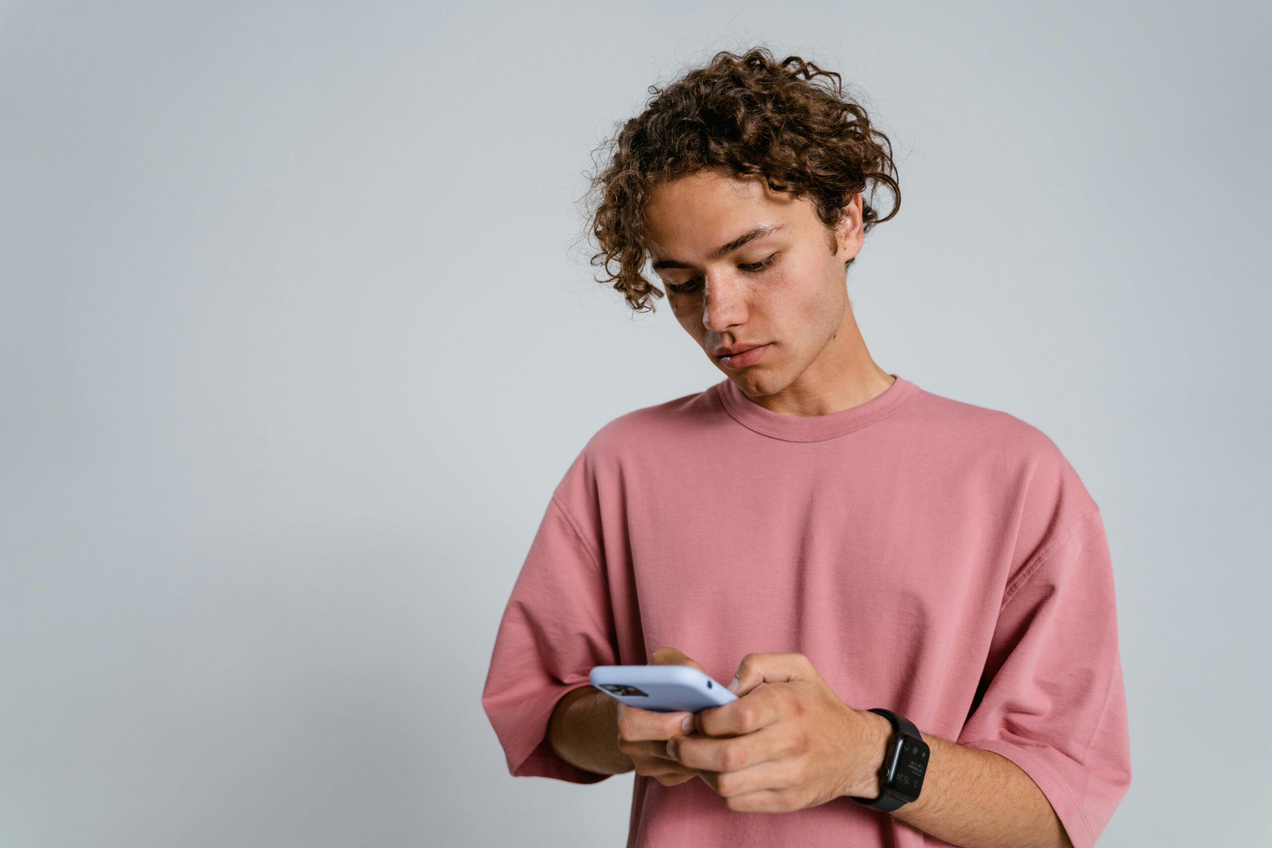 Adolescent boy looking down at his smartphone, illustrating how digital overstimulation impacts teen behavior.